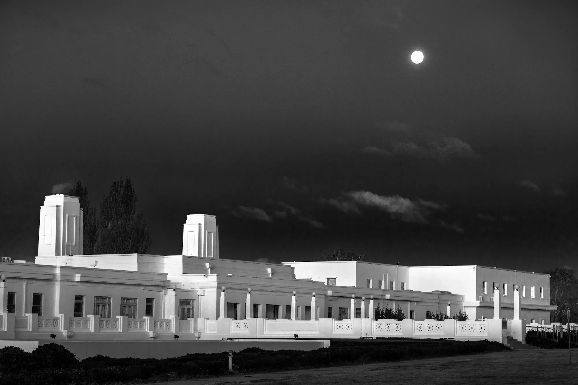 A long white building, Old Parliament House, with a dark sky and the moon in the background.