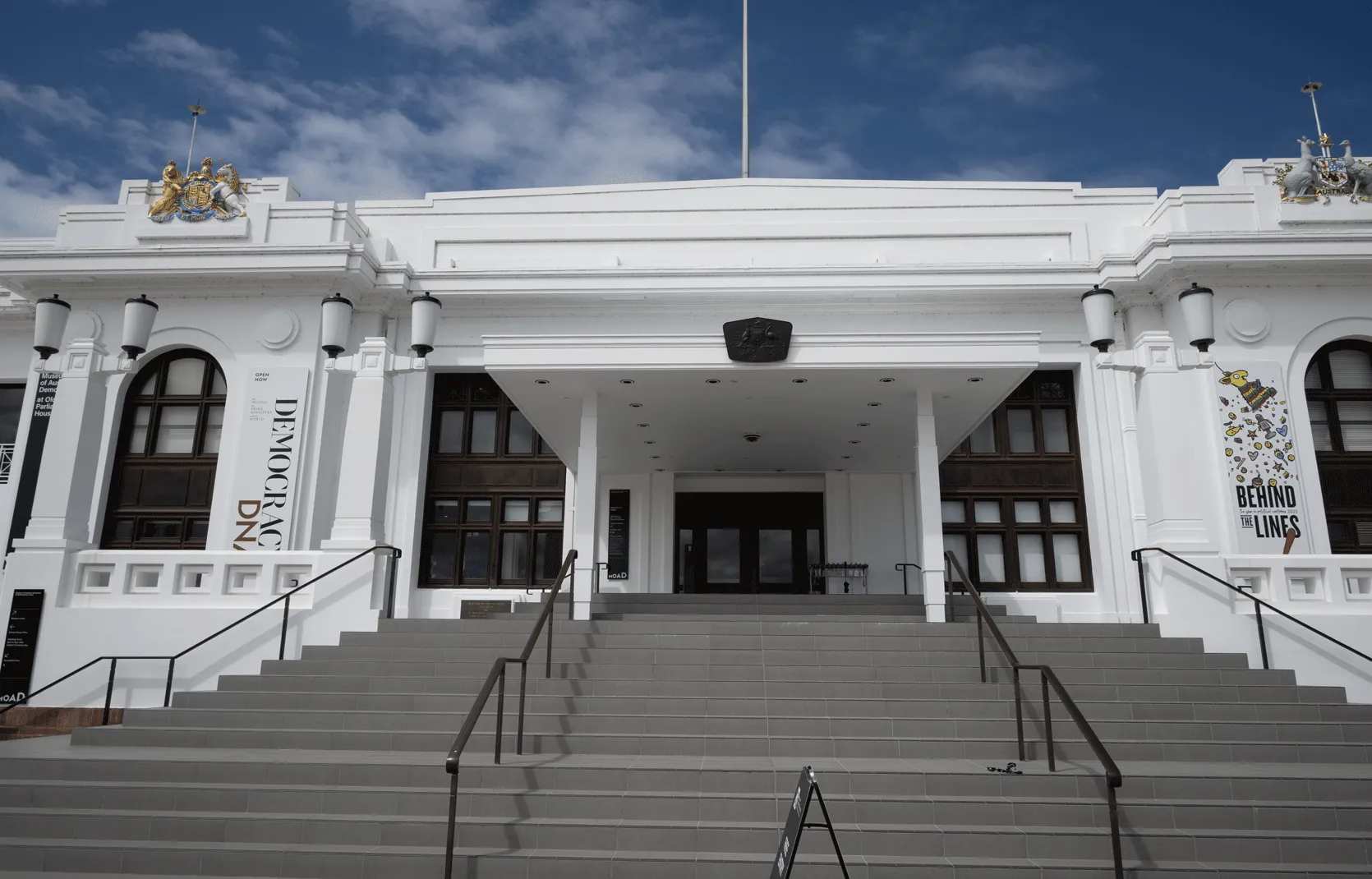 A large staircase leading up a large white building with two banners on either side. One reads 'Democracy DNA' and the other reads 'Behind the Lines'.