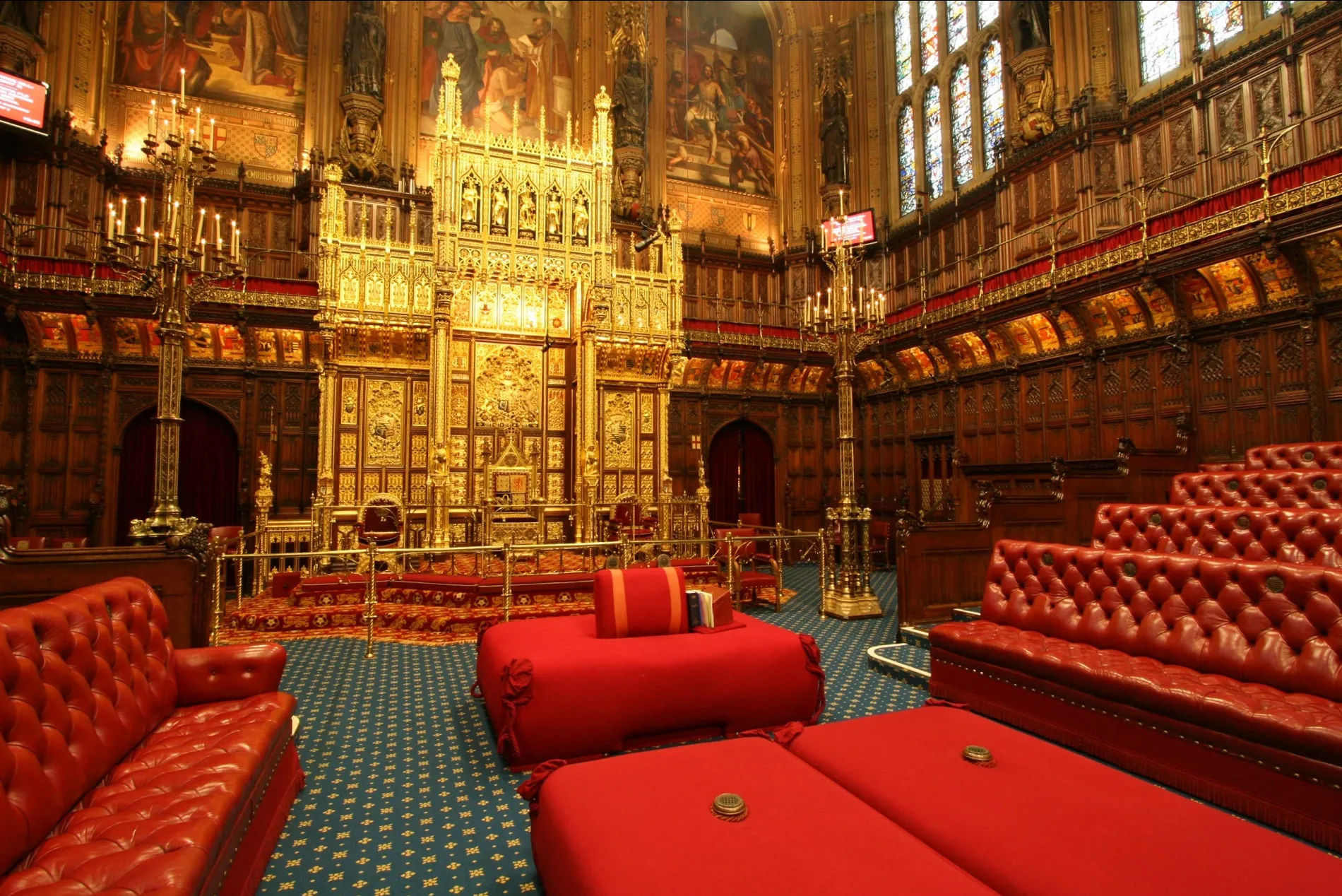 The House of Lords at Westminster, with a golden throne, red leather benches on each side, and big red cushions in the middle.