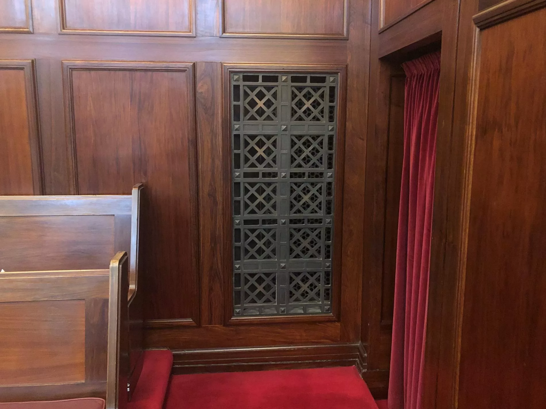 Rectangular bronze vent cover with a diagonal square pattern, inset in a wooden panelled wall.