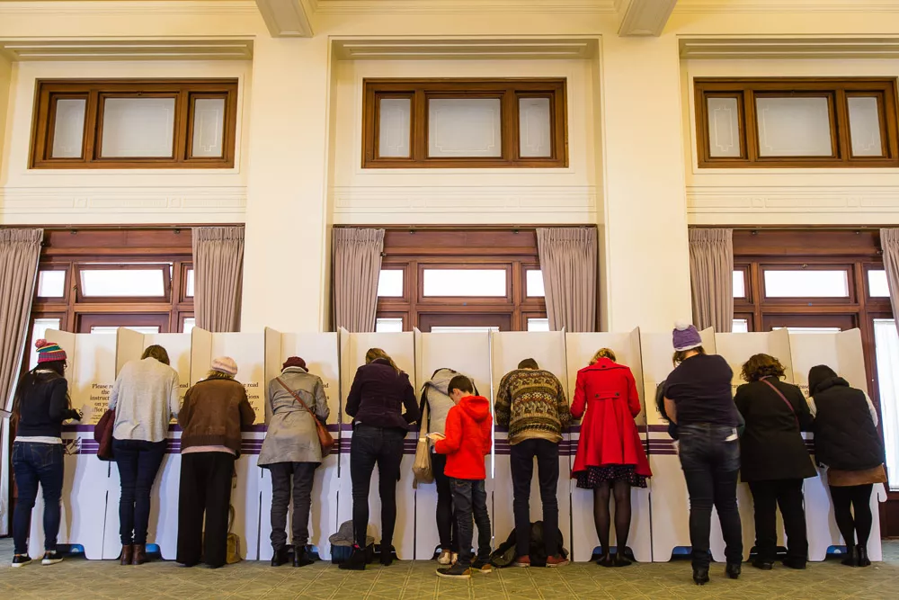 The backs of 10 people leaning filling out voting cards at MoAD.