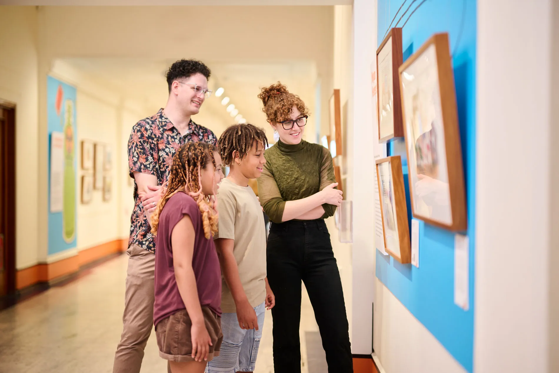 A smiling man, woman and two kids stand in a corridor at Old Parliament House looking at a political cartooning exhibition.