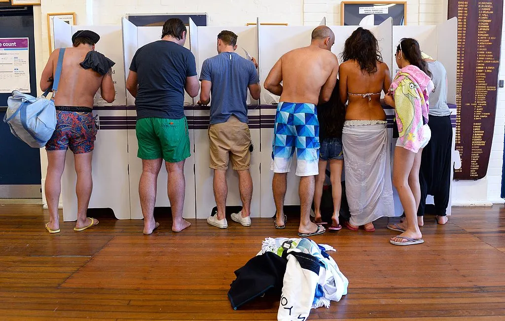 People wearing colourful boardshorts and beachwear stand at polling booths at a polling station in Sydney's Bondi Beach.