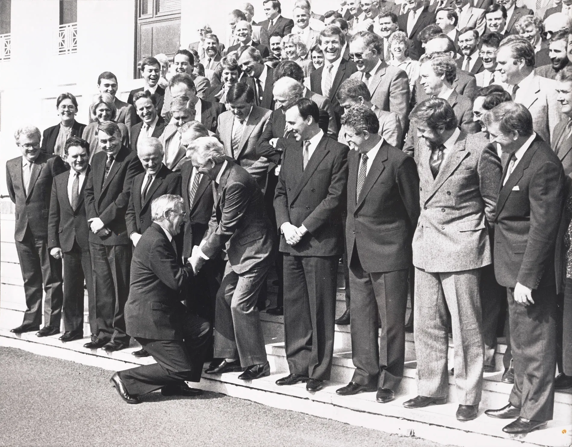 Bill Hayden curtsies to Bob Hawke who stands with other parliamentary staff on the steps of Parliament House.