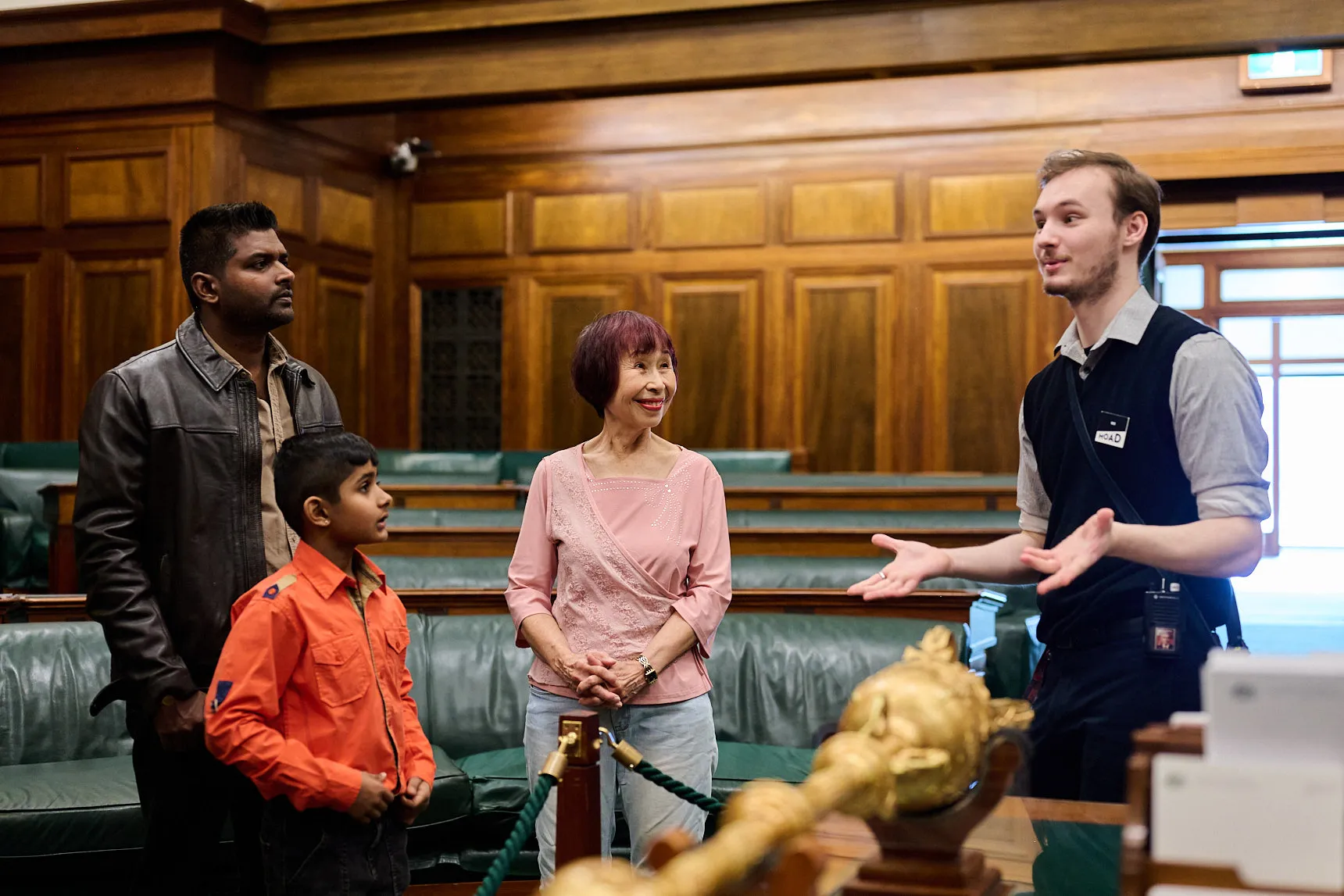 Three people and a tour guide stand in the House of Representatives Chamber in Old Parliament House.