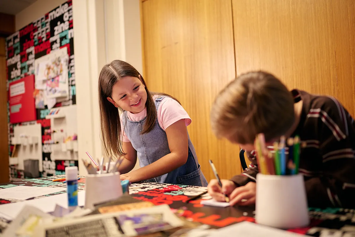 Two kids creating zines in the Zine Lounge, laughing with each other.