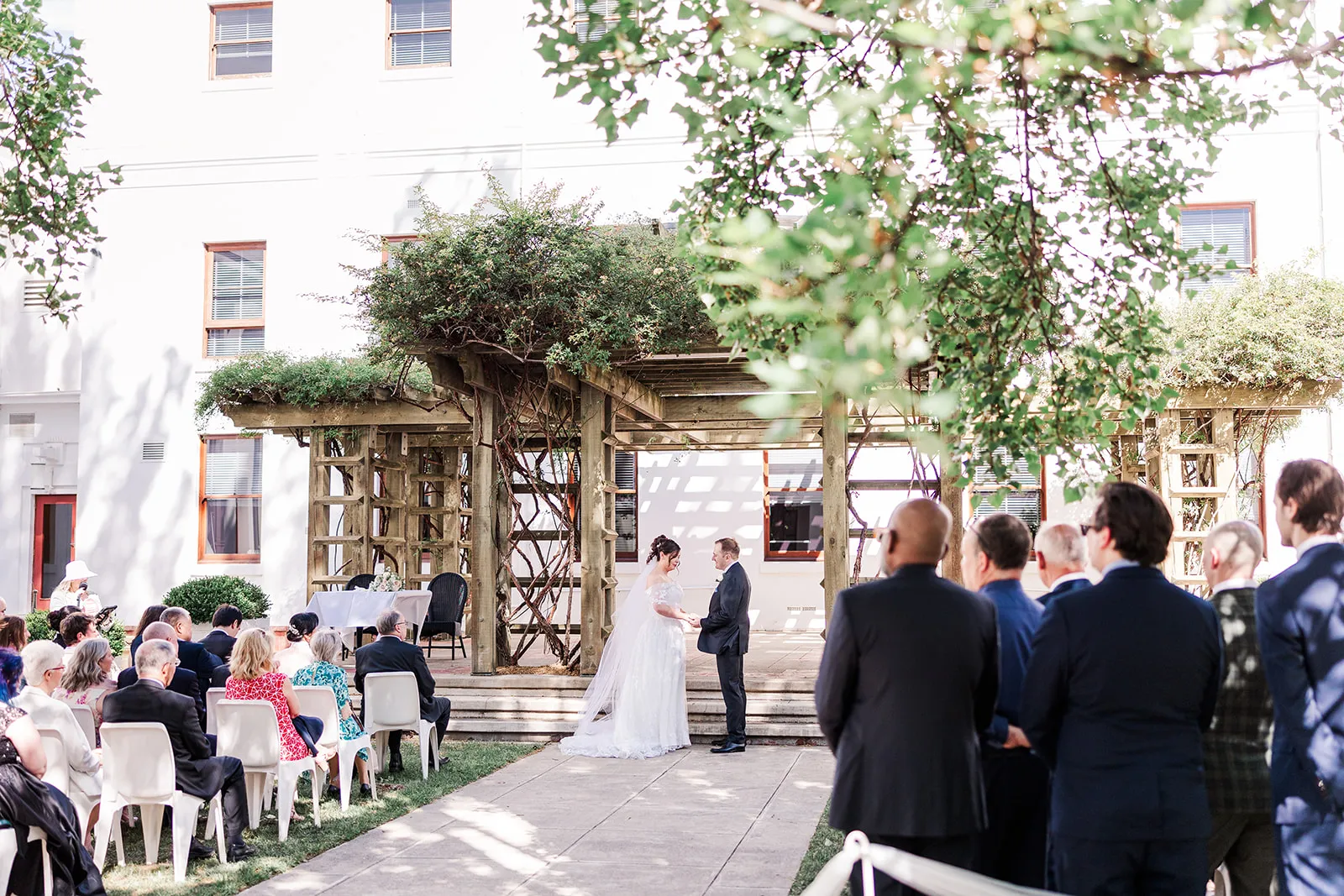 A wedding being held in the House of the Senate courtyard, the bride and groom are standing, looking at each other while holding hands.