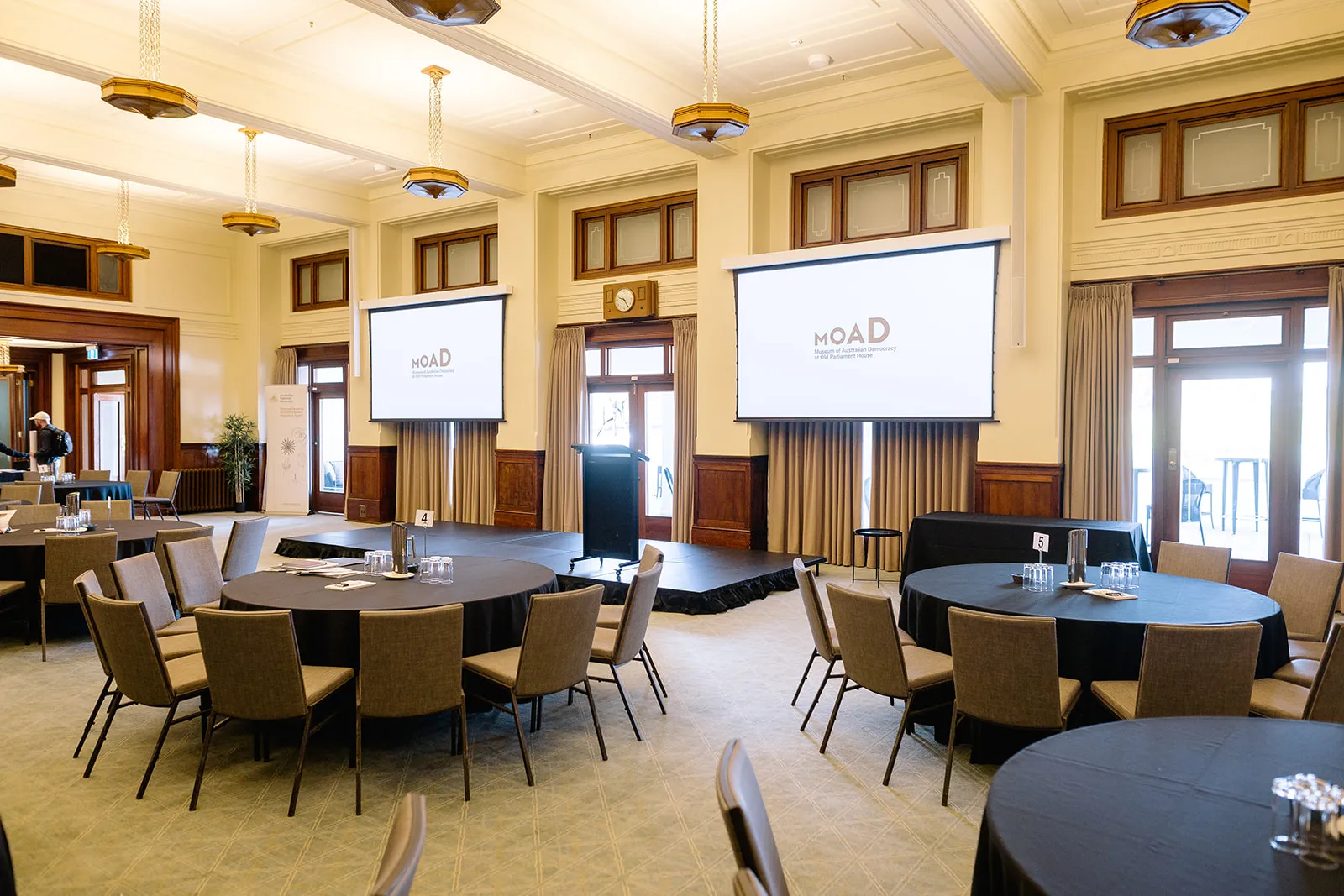 The Members' Dining Room set up with circular tables with chairs around them in front of a stage with a lectern on it.