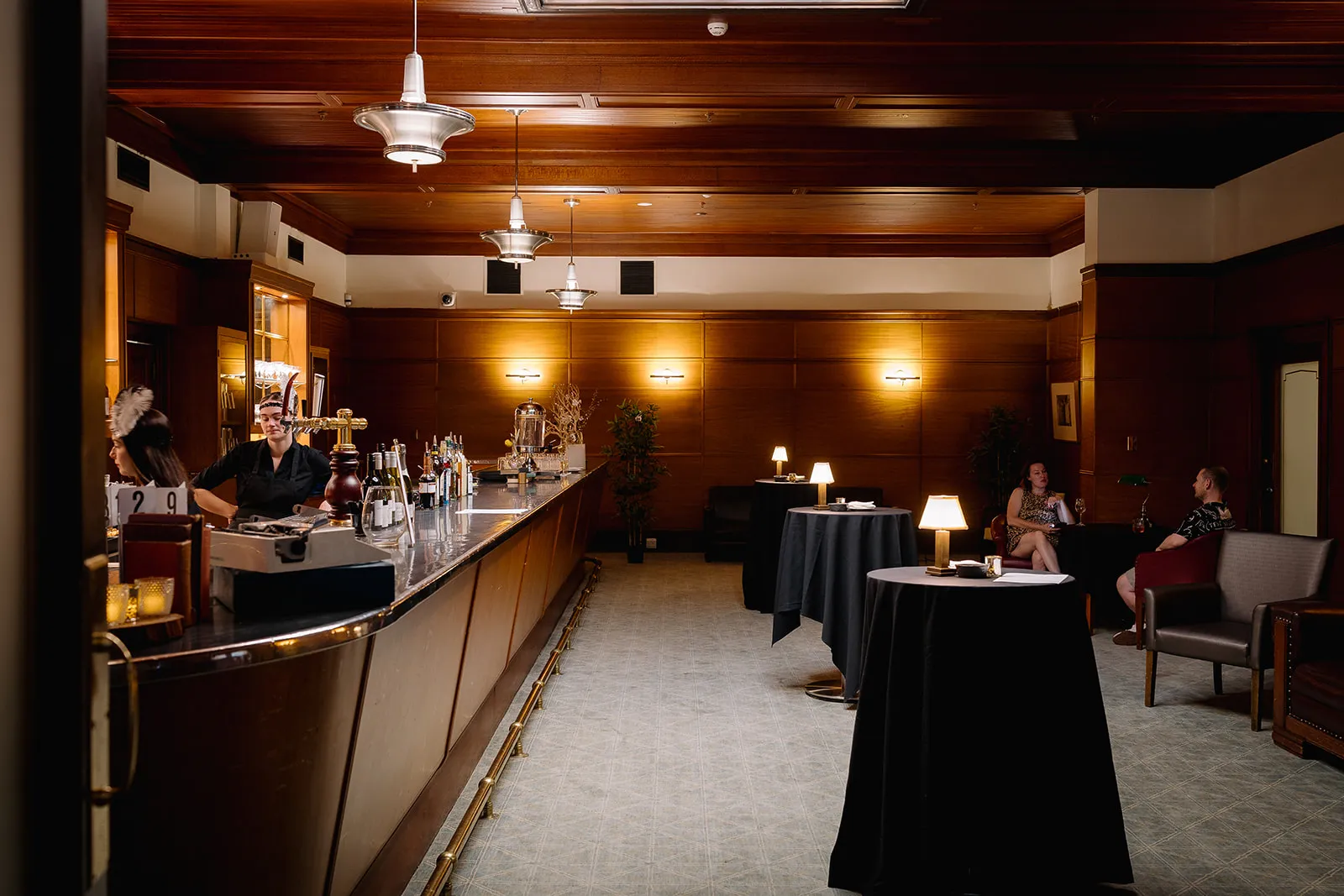 The Members' Bar being dimly lit, a couple of people are off at one of the tables talking to each other.