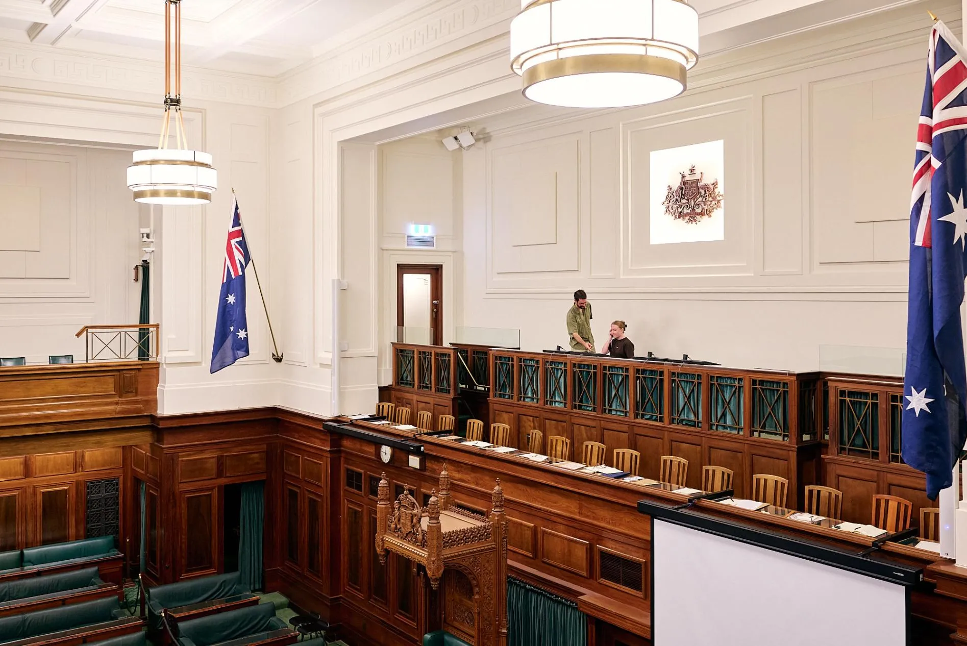 Two people sit in the Press Gallery in the House of Representatives Chamber in Old Parliament House.