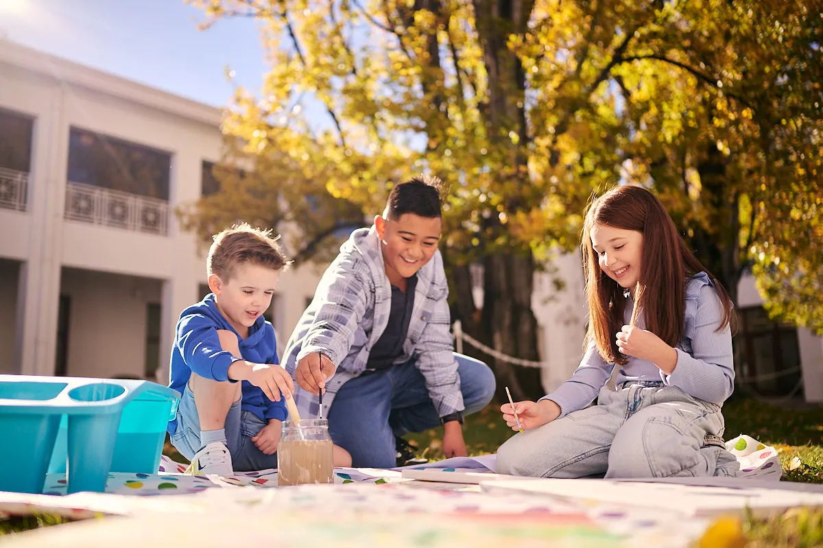 Three kids paint on a canvas in the House of Representatives Courtyard at Old Parliament House.