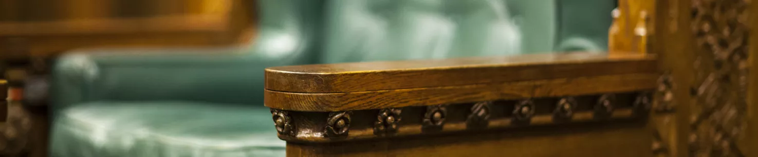 A close up of a large chair that is wooden, leather and ornate.