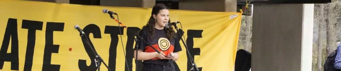 Dhani Gilbert speaks into a microphone, on stage, for a school strike for climate change protest