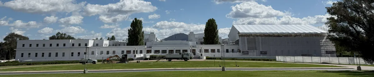 A view of the back of Old Parliament House, a long white building with a white scaffolding over one section of the roof and walls. 