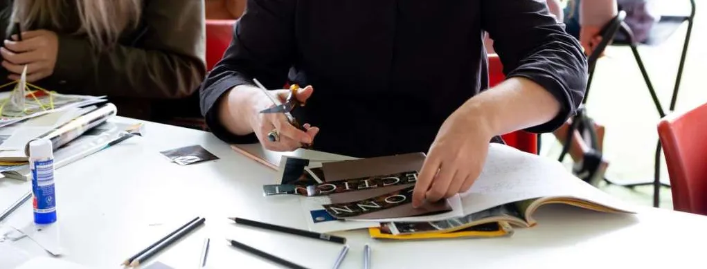 People sitting at a table, cutting pictures and titles out of magazines.