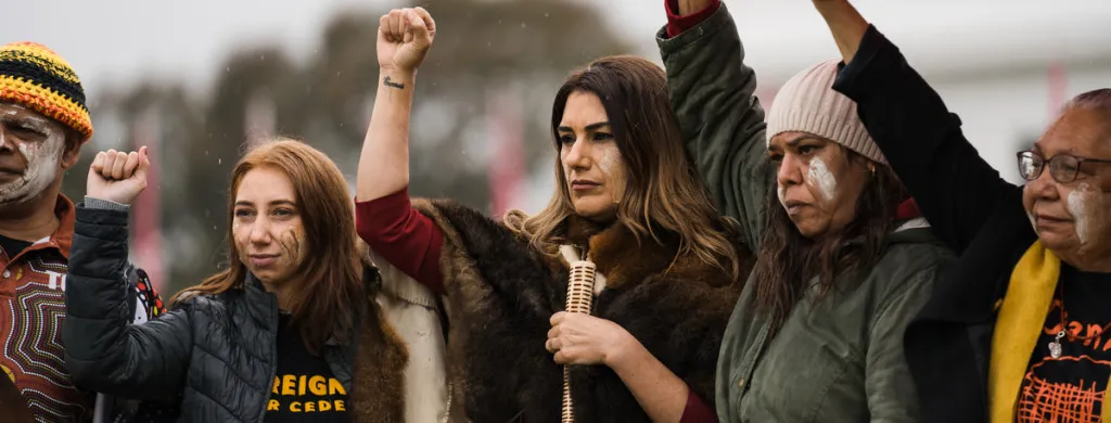 Left to right, Uncle Billy T Tompkins, Leah House, Senator Lidia Thorpe, Diyan Coe, Aunty Matilda House and Dhani Gilbert all holding their fists raised in light rain. 