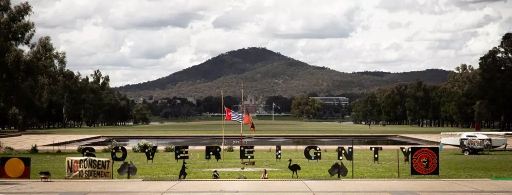 The site of the Aboriginal Tent Embassy on the lawns outside Old Parliament House. Black letters spell out the word 'Sovereignty' on a green lawn.