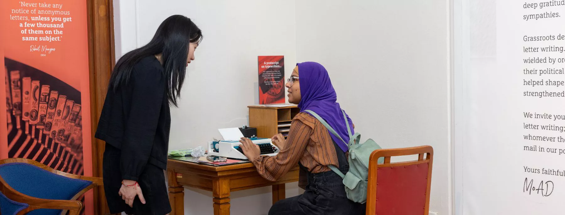 A visitor sat at a desk while tlaking to another visitor