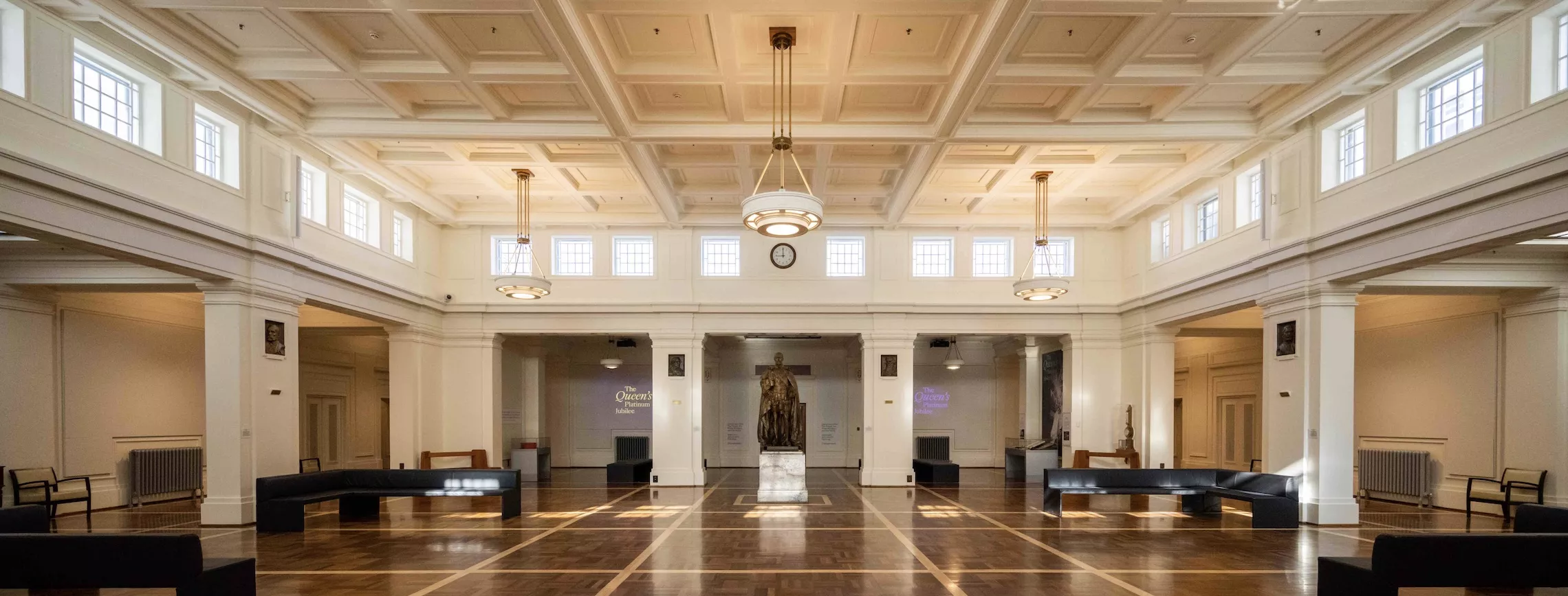 A bronze statue of a man is the focal point of a hall with a timbered floor and white columns.