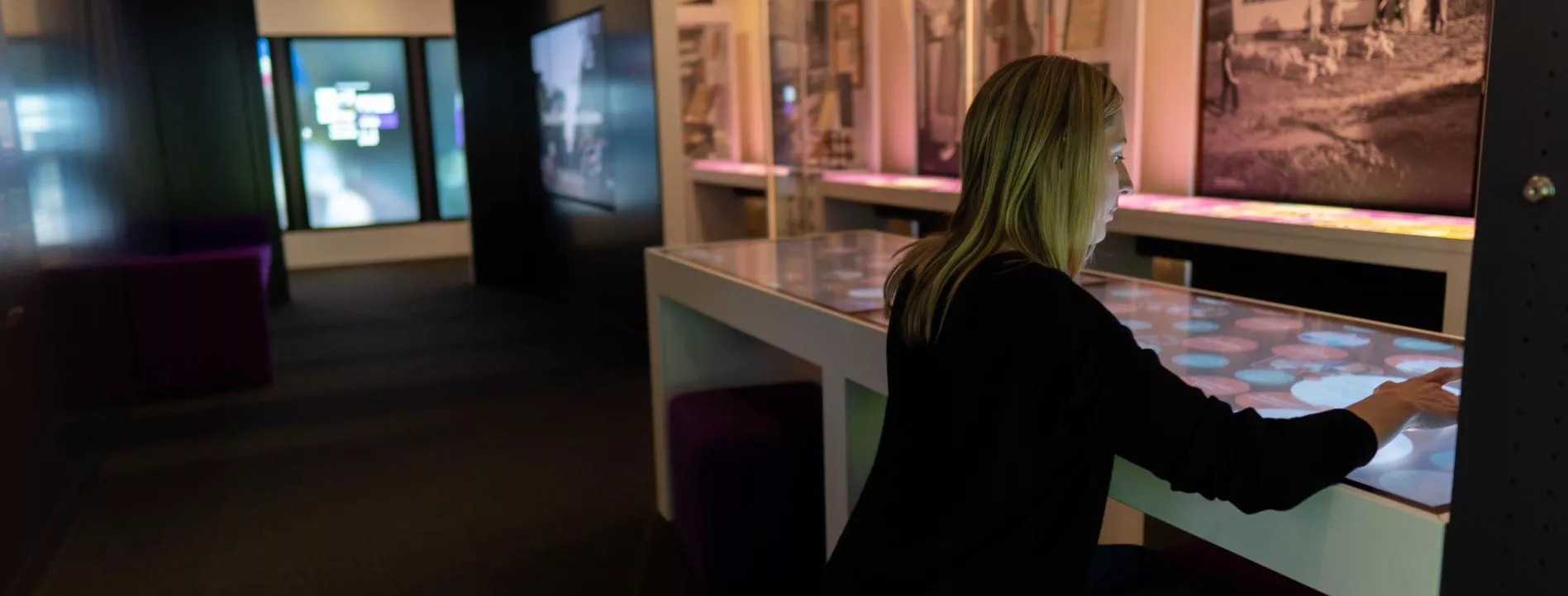 A woman is sitting and interacting with a touchscreen in an exhibition