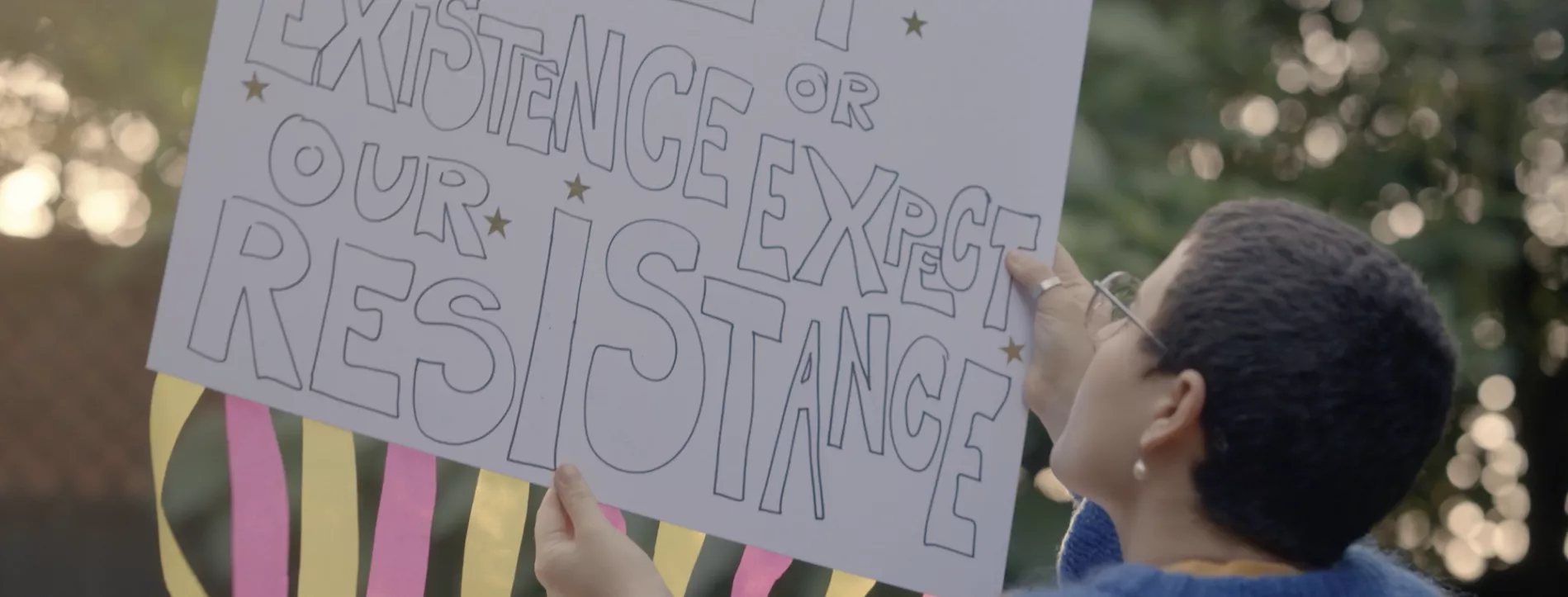 A person holds up a protest placard with the label "Respect our existence or expect our resistance"