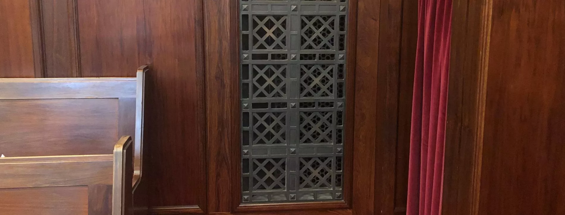 Rectangular bronze vent cover with a diagonal square pattern, inset in a wooden panelled wall.