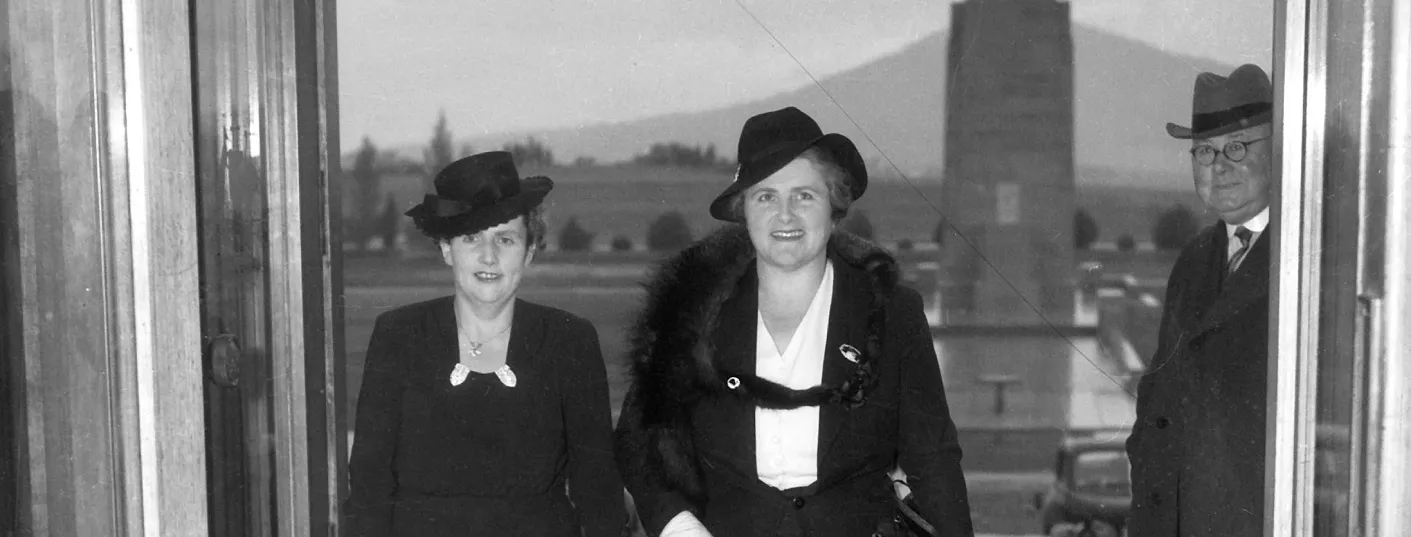 Dorothy Tangney and Enid Lyons walk together through the front door of Old Parliament House, smiling.