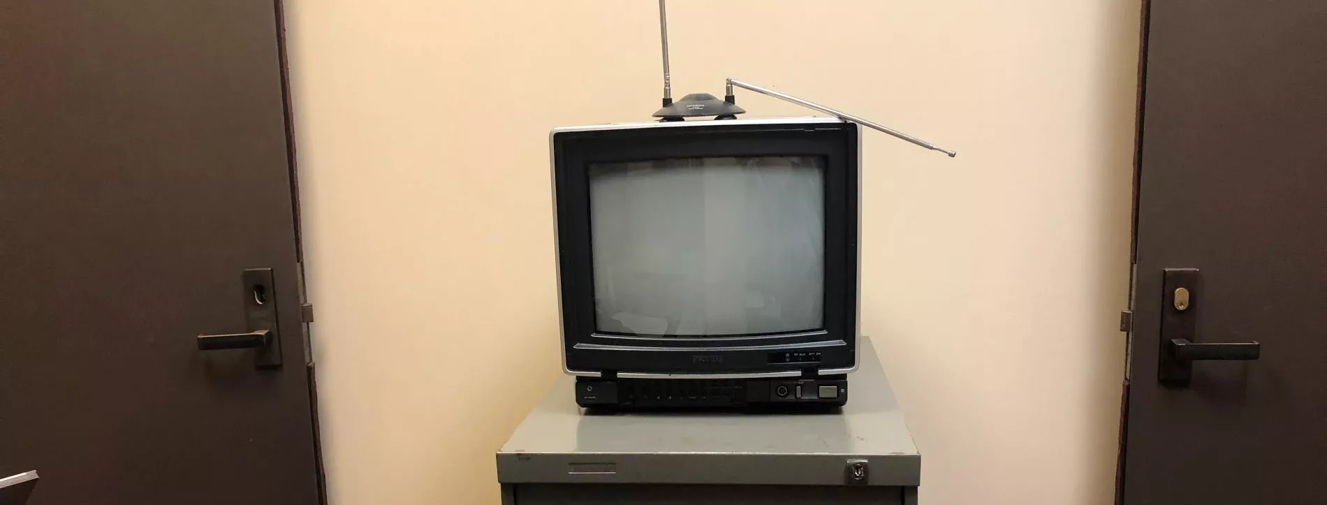 A small television with an aerial antenna sits on top of a grey filing cabinet.