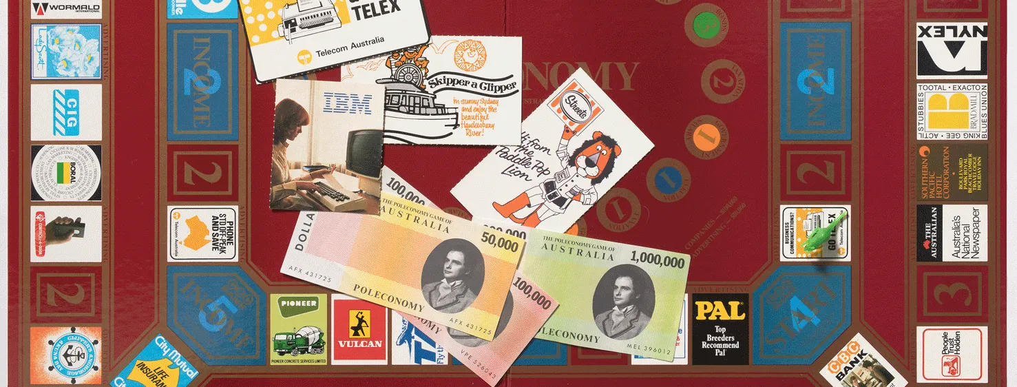 A board game with a dark red board opened up with a row squares around the outside of the board with the names of different companies such as Kodak, Hoyts and Newsweek. In the centre are some game pieces including 3 pieces of paper representing money and some cards with businesses on them including IBM and Telecom. 