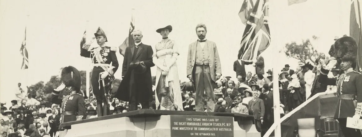 Governor-General Denman, Prime Minister Fisher, Lady Denman and King O'Malley stand on a commemorative stone. British and Australian flags are the in background, with a large crowd behind.