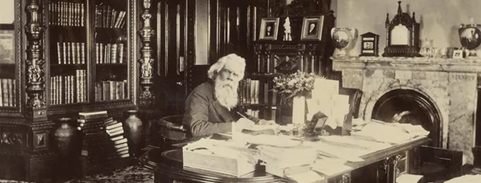 Sir Henry Parkes sits at his desk, with papers and books scattered throughout the room. 