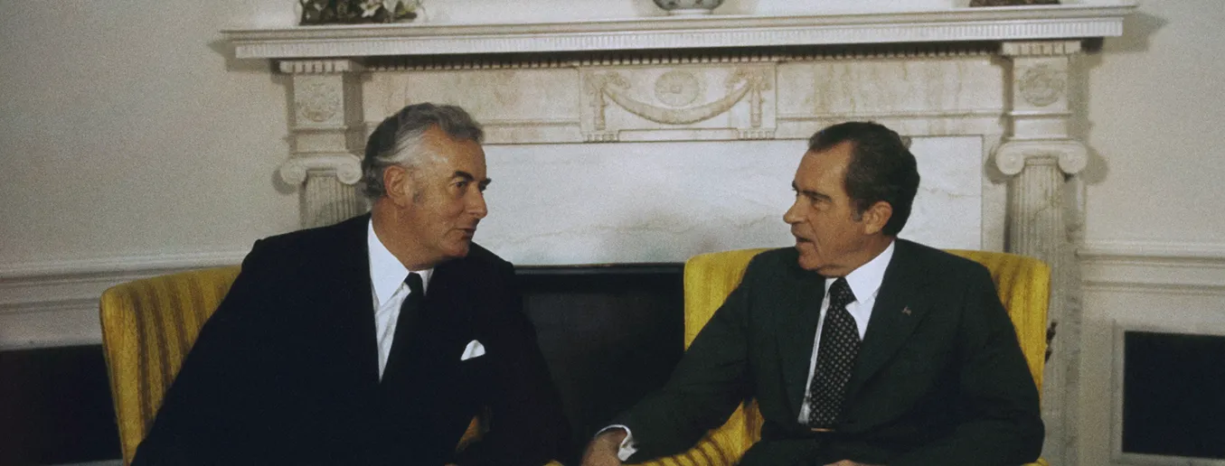 Richard Nixon and Gough Whitlam sit in yellow chairs in the Oval Office facing each other and talking.