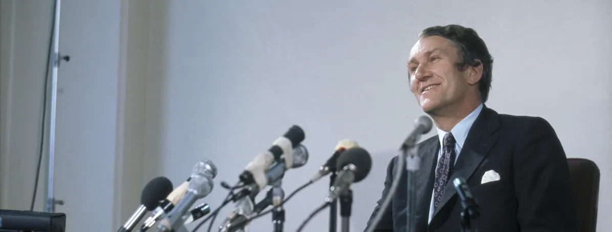 Malcolm Fraser looks out from behind a desk with microphones on it.