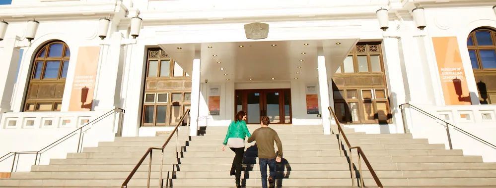 Two people walk up the front entrance steps of Old Parliament House.