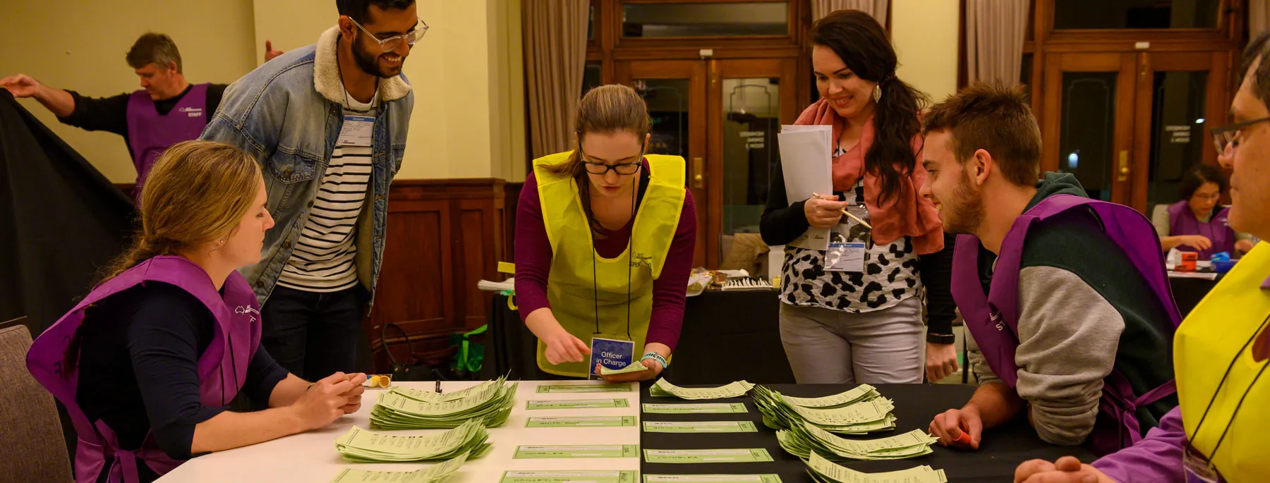 Officials in yellow and purple vests count green ballot paper votes on a table in Old Parliament House.