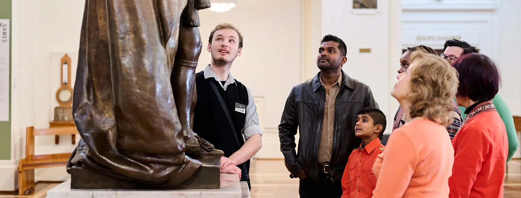 People stand in a group in King's Hall in Old Parliament House looking at a bronze statue of King George.