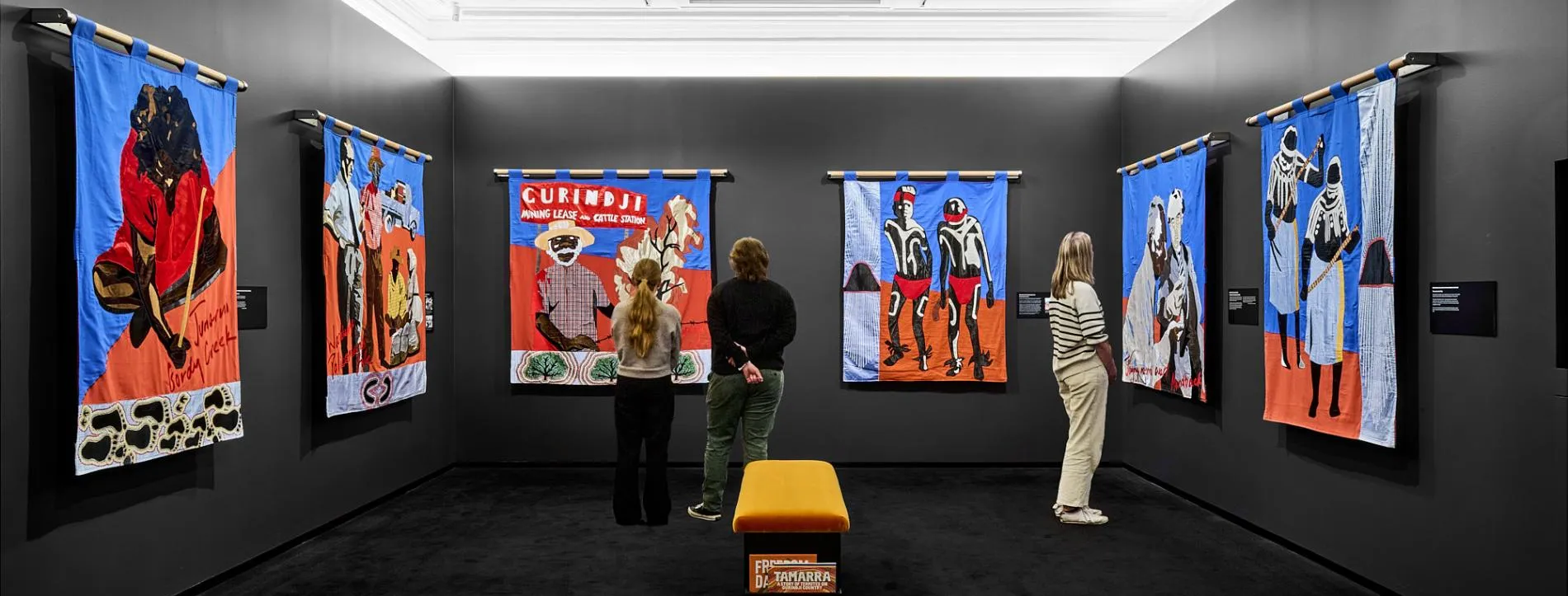 Three people stand looking at the Gurindji freedom banners exhibition in Old Parliament House.