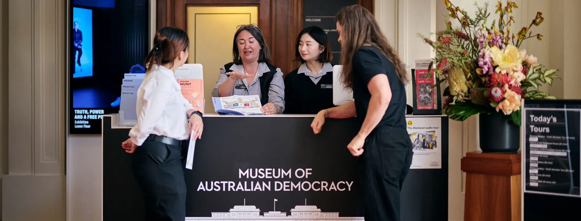 Museum staff show visitors to a brochure at the reception desk at MoAD at Old Parliament House.