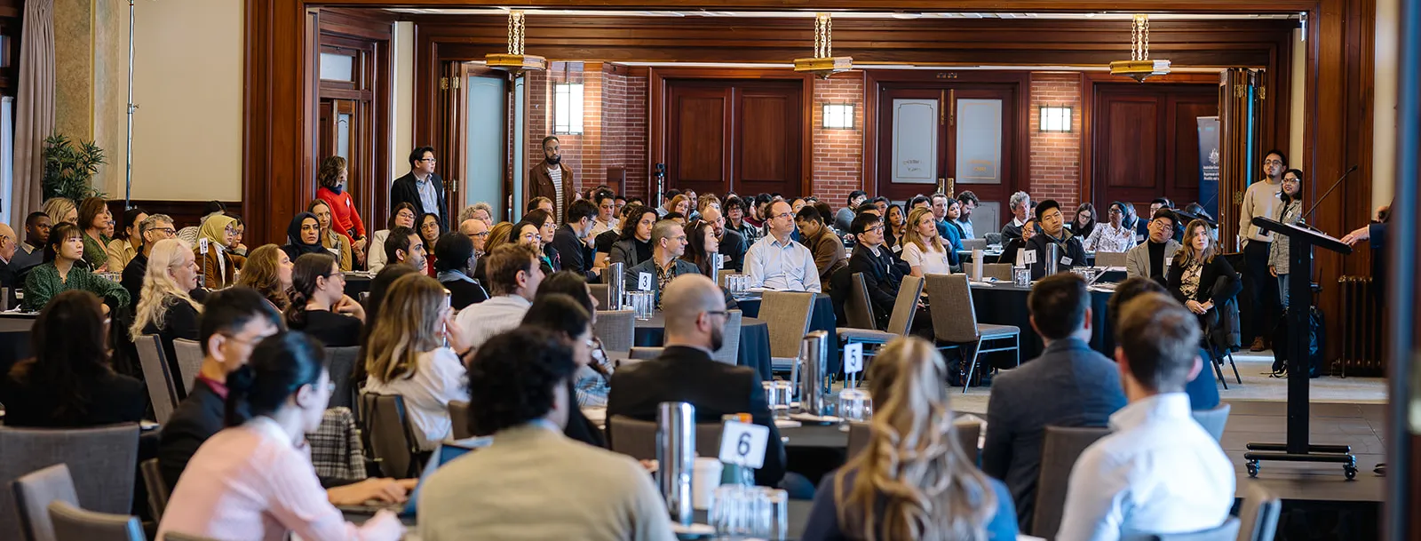 People seated at tables in the Member's Dining Room, facing a lectern where someone is giving a presentation.
