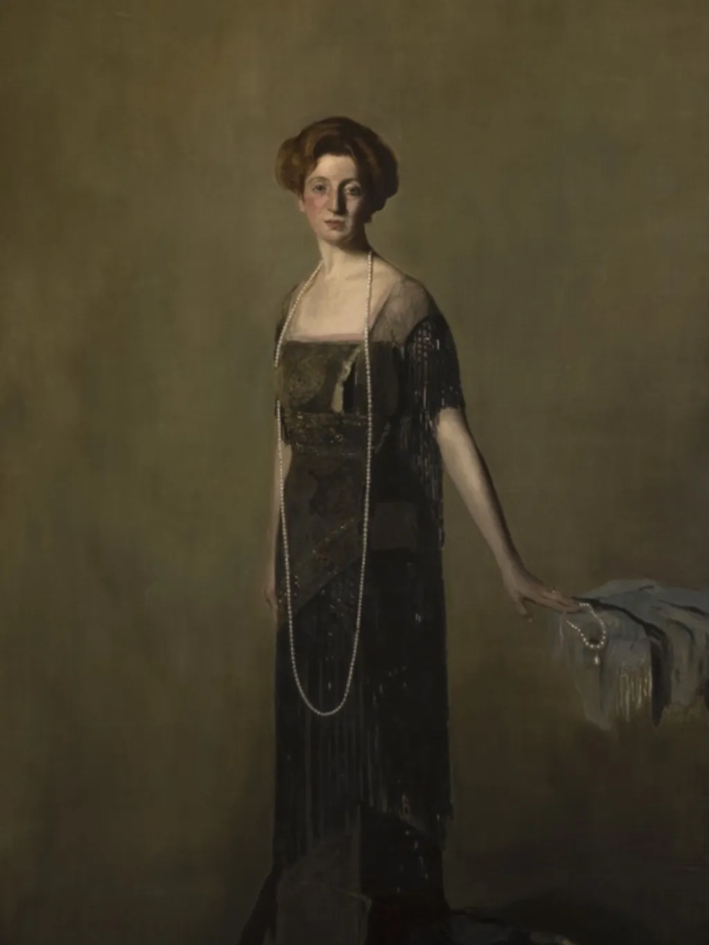 Lady Denman, with short brown hair, wearing a long dark dress and a long pearl necklace that drapes down to knee height.