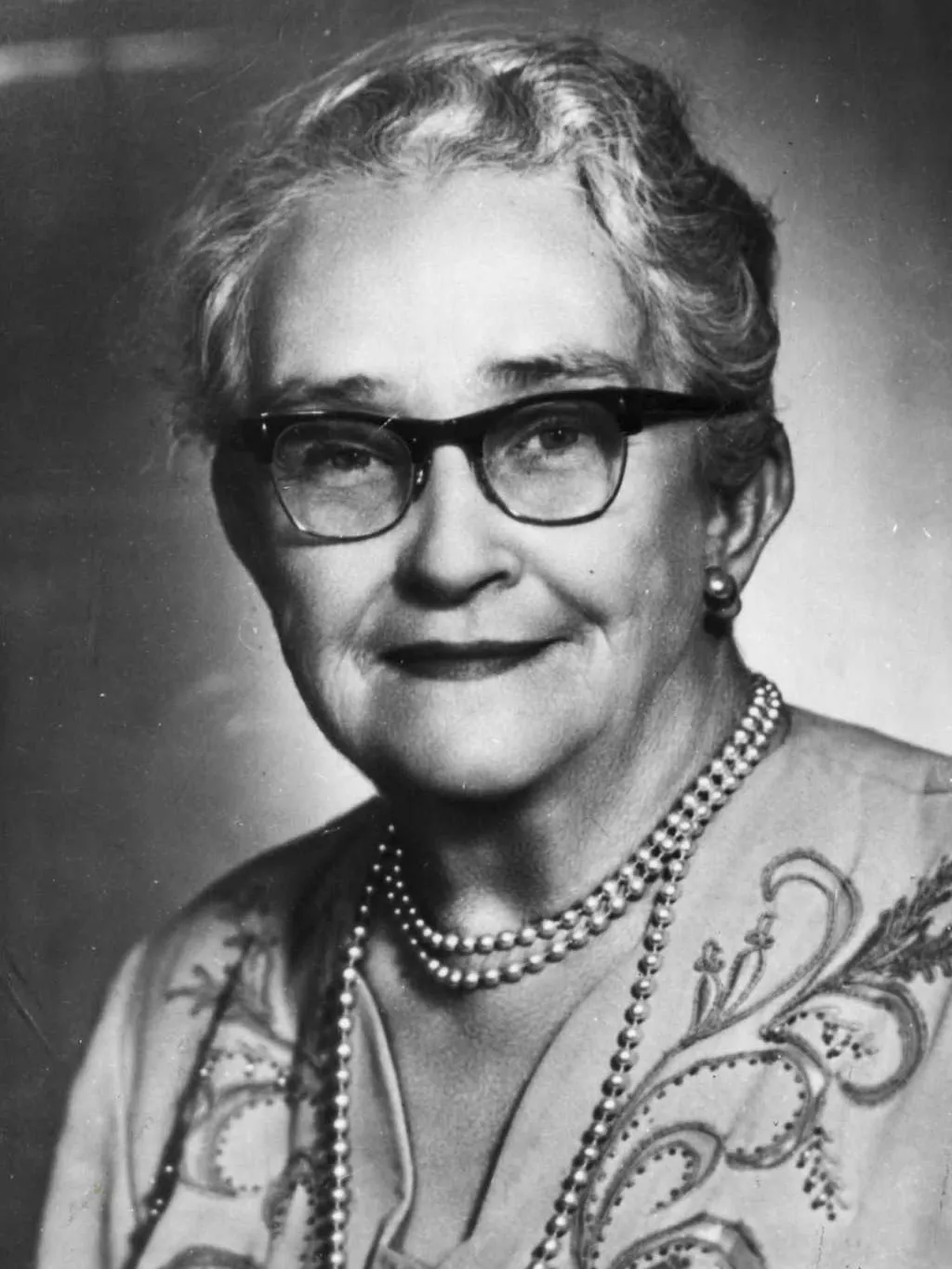 Senator Agnes Robertson, wearing thick-rimmed glasses and pearl earrings and necklace.