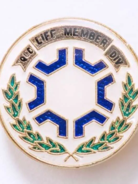 A round pin with a laurel wreath, a pattern of blue shapes, and the words 'Life Member, QLD Div'.