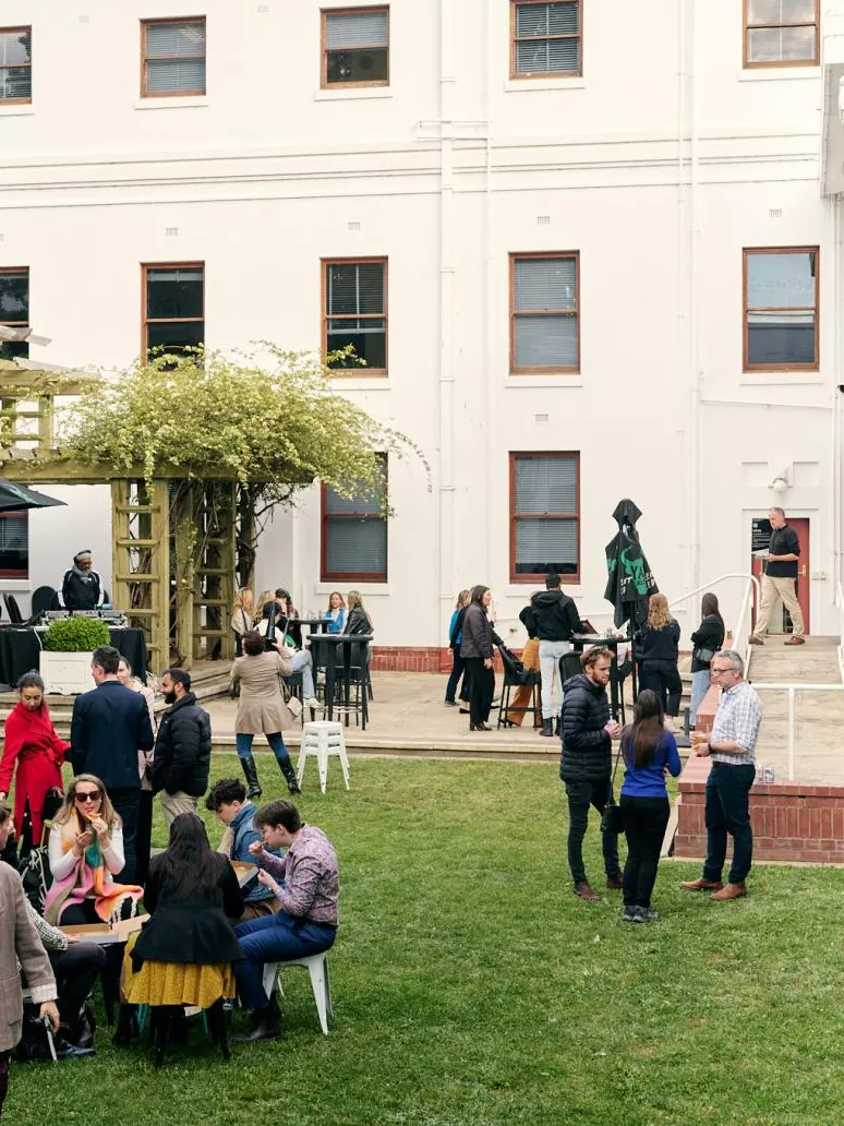 A large enclosed grassed area, the House of Representatives courtyard, with many groups of people gathered, talking, eating and drinking.