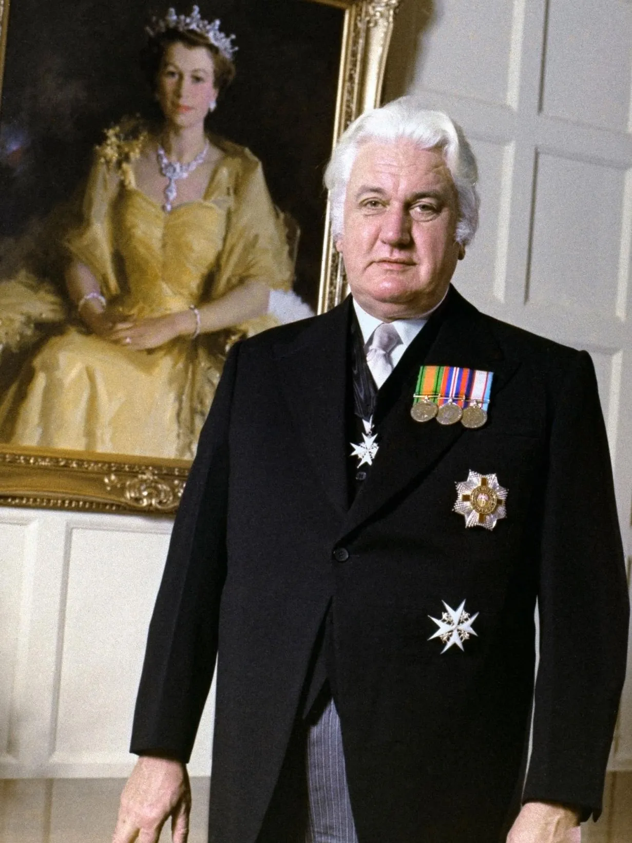 Sir John Kerr dressed in a morning suit stands in front of an oil painting of Queen Elizabeth II.