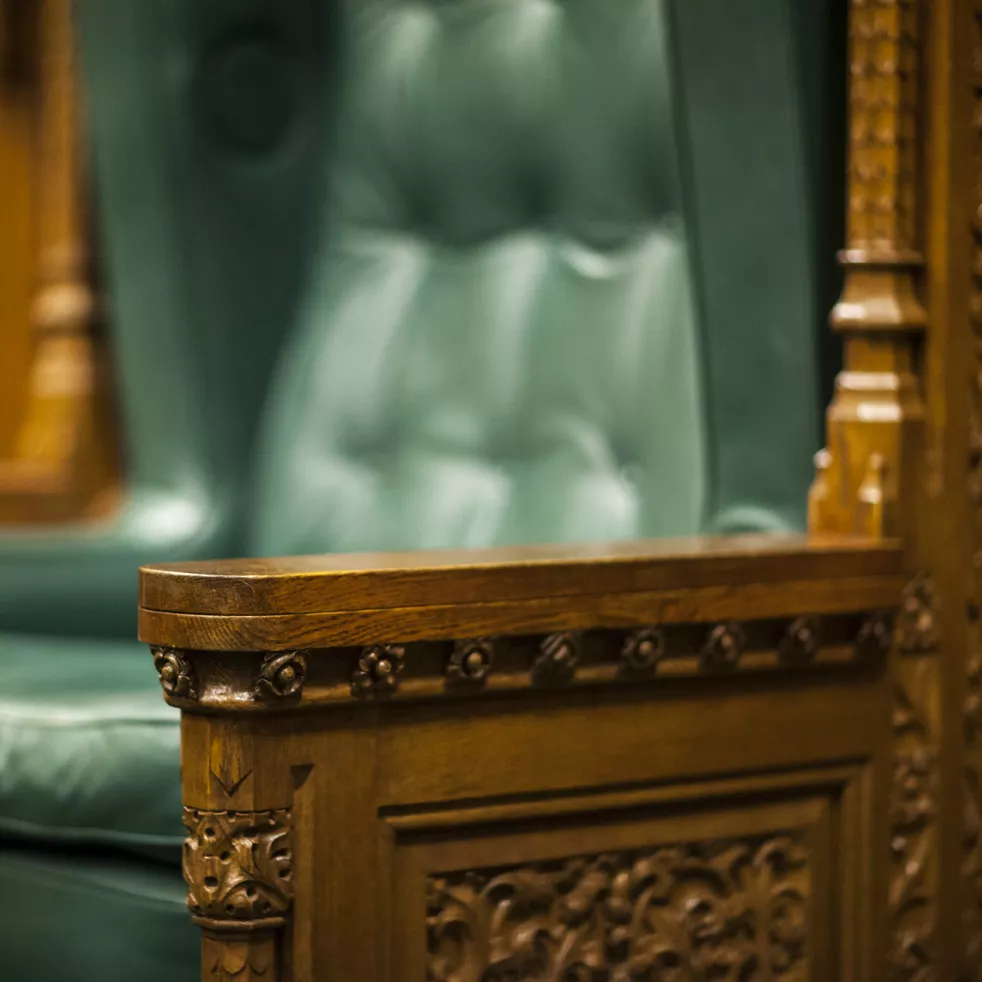 A close up of a large chair that is wooden, leather and ornate.