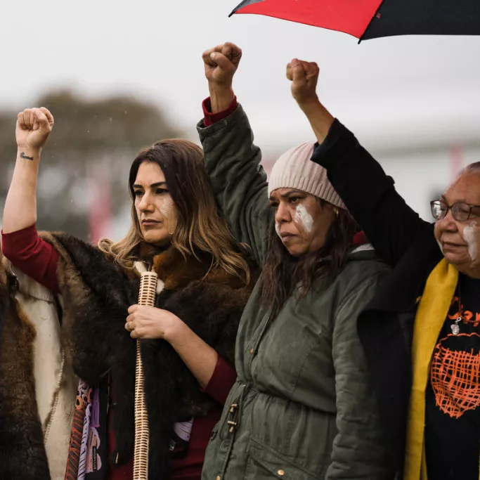 Left to right, Uncle Billy T Tompkins, Leah House, Senator Lidia Thorpe, Diyan Coe, Aunty Matilda House and Dhani Gilbert all holding their fists raised in light rain. 