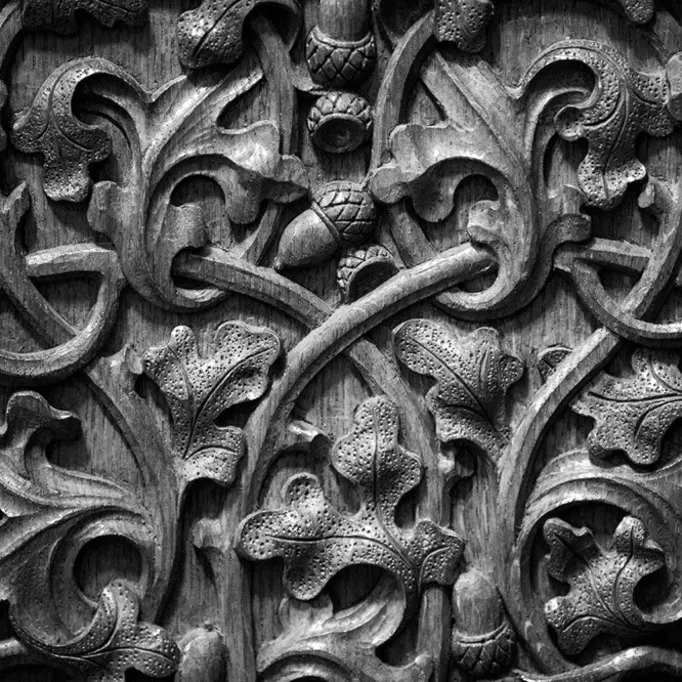 Black and white close-up photo of oak leaf and acorn shaped carvings into a wooden panel.