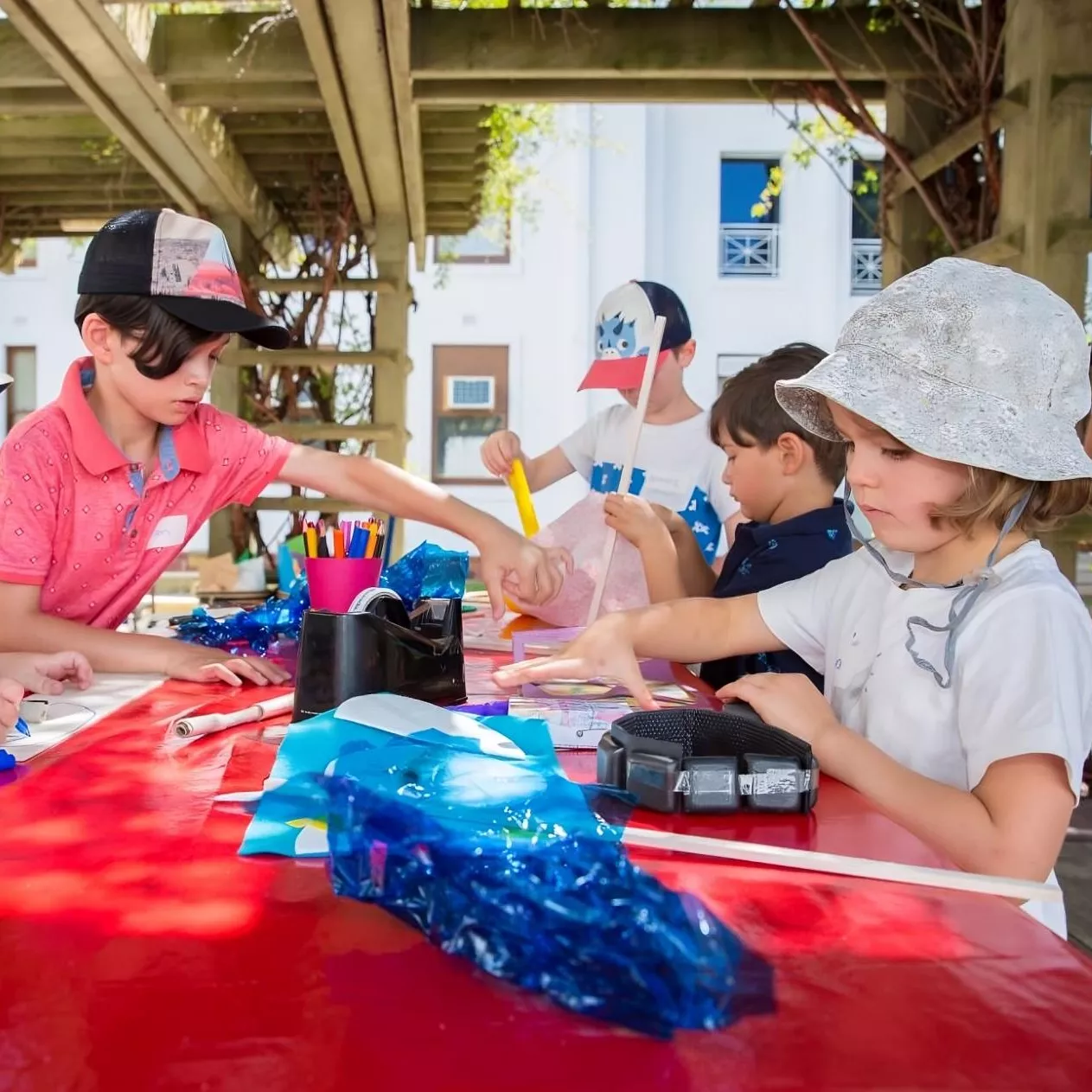 Four children stand around a table outdoors, each focusing on an idividual craft project.