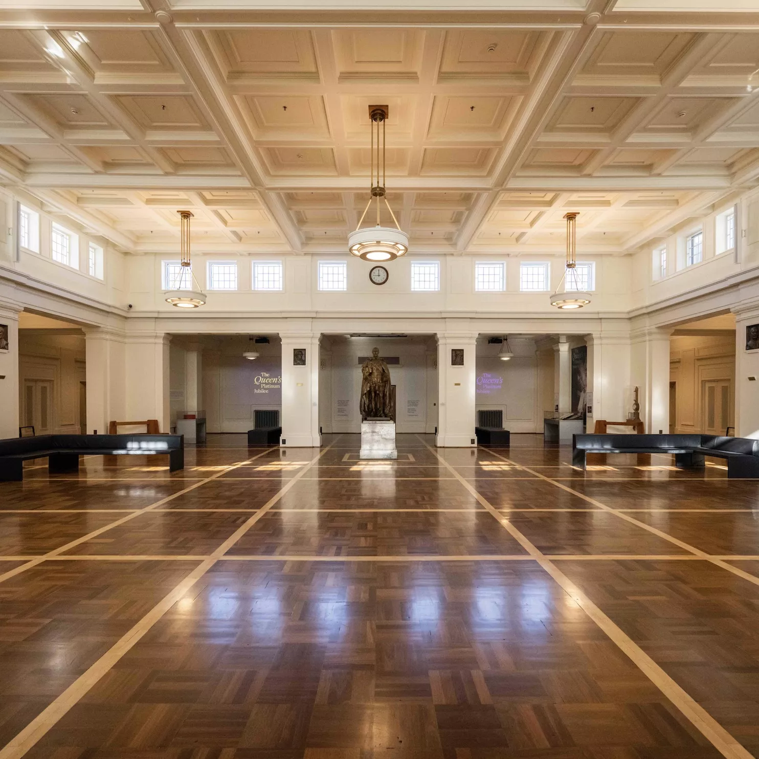 A bronze statue of a man is the focal point of a hall with a timbered floor and white columns.