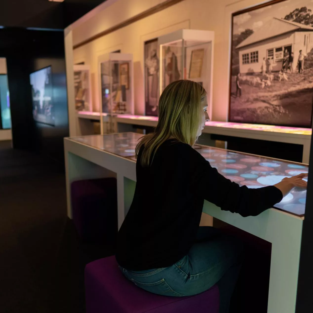 A woman is sitting and interacting with a touchscreen in an exhibition